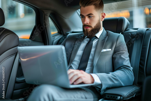 Handsome businessman working on laptop computer while sitting in luxury car. © Mayava
