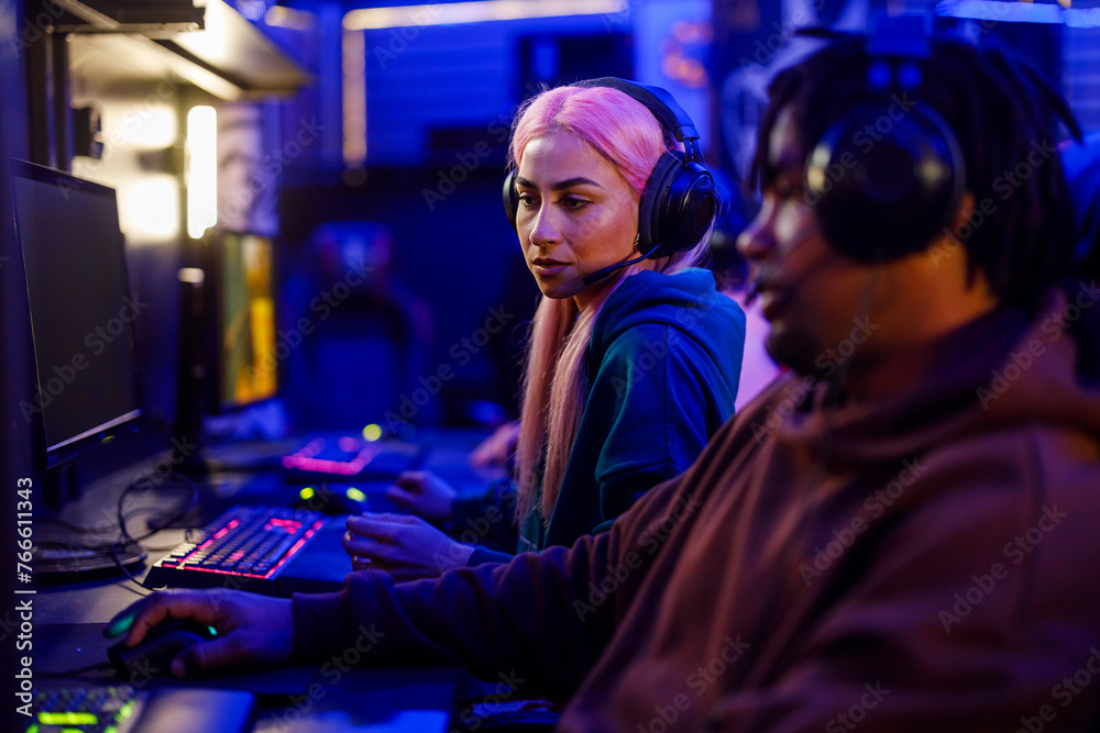 Female with pink hair gamer looking at her friend screen while playing a game Female with pink hair gamer looking at her friend screen while playing a game