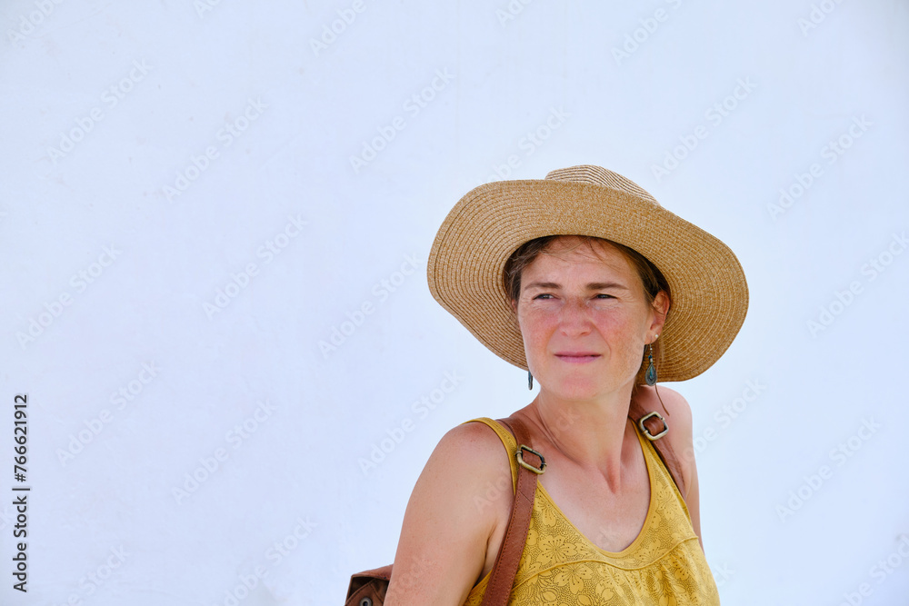 Dreamy woman in summer hat looking away against white wall