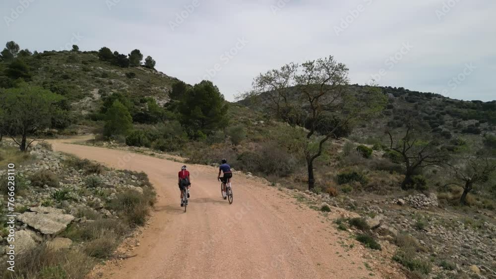 Aerial drone view of cyclists are riding gravel bikes in the scenic beauty of the Spanish mountains in cloudy day. Cycling on gravel road or off-road. Gravel bike riding in nature. Aerial drone view of cyclists are riding gravel bikes in the scenic beauty of the Spanish mountains in cloudy day. Cycling on gravel road or off-road. Gravel bike riding in nature.