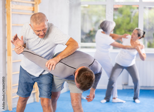 Self-defense lesson - elderly man twists the arm of attacking man with painful hold in gym