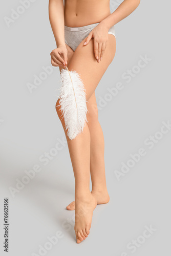 Young woman with soft feather on grey background. Epilation concept