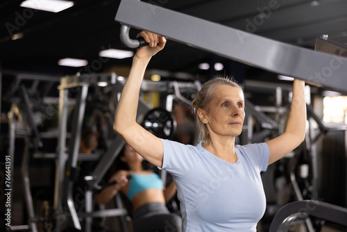 Mature female athlete working out at shoulder press machine in gym