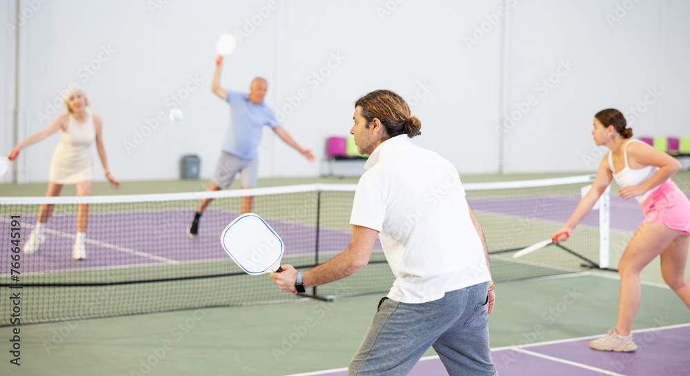 Rear view of focused adult man playing pickleball match on indoor court on blurred background of opponents. Sport and active lifestyle concept..