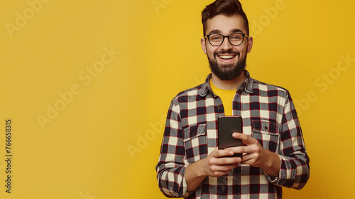 Young boy with glasses smiling and looking at the camera, holding a phone in his hands, yellow background for commercial and text
