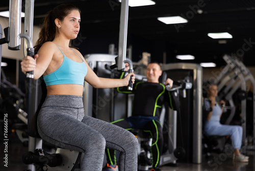 Sporty young woman using chest fly machine in gym