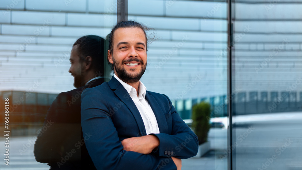 Confidence successful businessman in suit with beard standing in front of office glass building lean on wall arm crossed looking at camera and smile. Hispanic modern business man portrait. Banner Confidence successful businessman in suit with beard standing in front of office glass building lean on wall arm crossed looking at camera and smile. Hispanic modern business man portrait. Banner