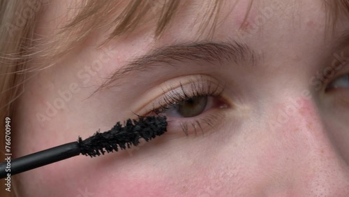 Woman is shown in an extreme close-up applying mascara to her brown eyes with the tip of brush to prevent clumping. Mascara may enhance and define appearance of eyes. Extreme close-up view process