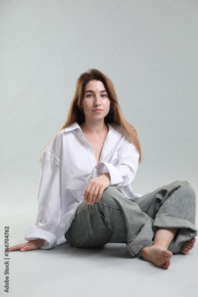 Portrait of beautiful young woman sitting on grey background Portrait of beautiful young woman sitting on grey background