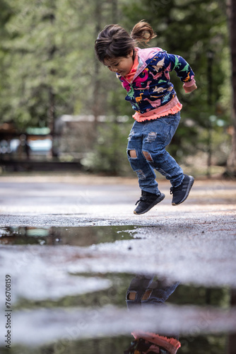 A young girl is jumping in a puddle of water