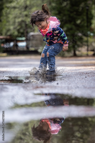 A little girl is playing in the rain and splashing in a puddle