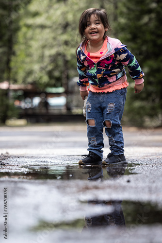 A young girl is standing in a puddle of water, wearing a blue and pink jacket