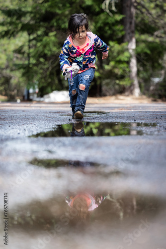 A young girl is walking on a wet road, with her reflection in the water