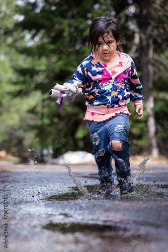 A little girl is running through a puddle of water, holding a stuffed animal