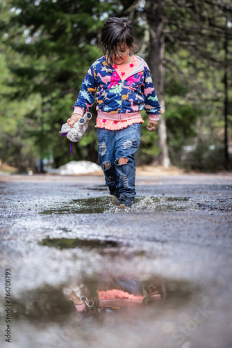 A young girl is walking through a puddle of water, holding a toy in her hand