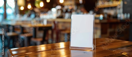 Label the empty menu holder at the bar restaurant with white paper inserts and tent card made of acrylic on a wooden table. Background of a blurred cafeteria allows for adding customer text. photo