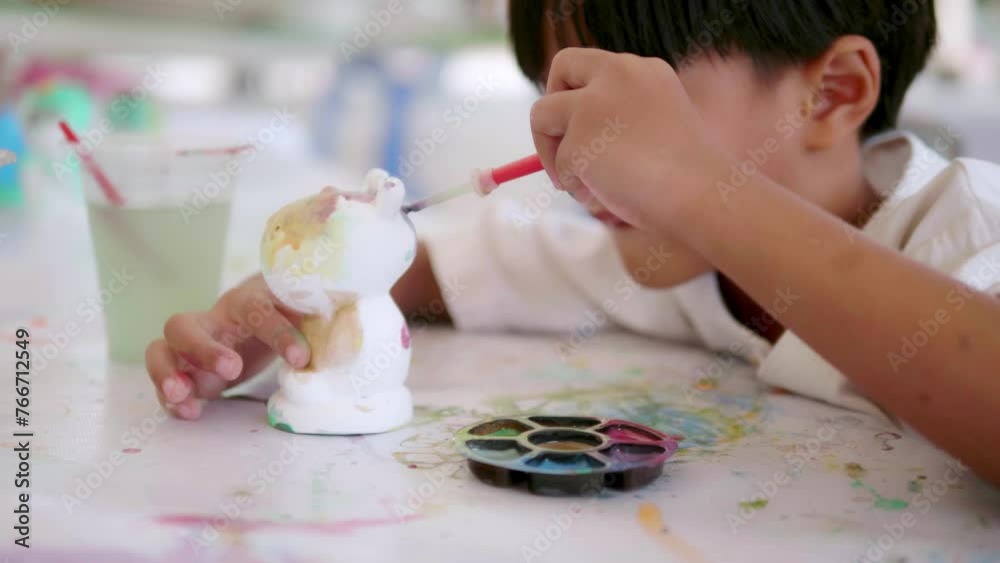 Cute Asian boy holding a paintbrush is painting watercolors on various shapes with preschool children, art class participants. Developing children's abilities, creative hobbies, day care activities Cute Asian boy holding a paintbrush is painting watercolors on various shapes with preschool children, art class participants. Developing children's abilities, creative hobbies, day care activities