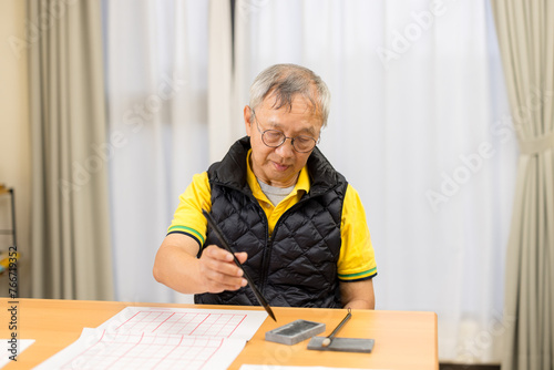 Asian old man write Chinese calligraphy character at home