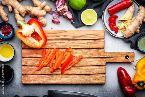 Food and cooking background. Gray table with chopped paprika. Zucchini, raw vegetables, spices and ingredients for cooking vegan Asian dishes with ginger, garlic, soy sauce, top view