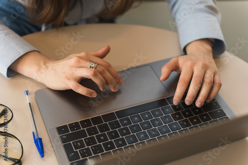 Close-up of the hands of a corporate woman dressed in a light blue formal shirt typing on her laptop
