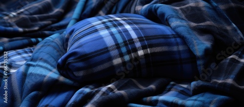 A close up of an electric blue plaid blanket on a bed, the intricate pattern contrasting with the darkness of the room. A human leg peeks out from under the comforting fabric