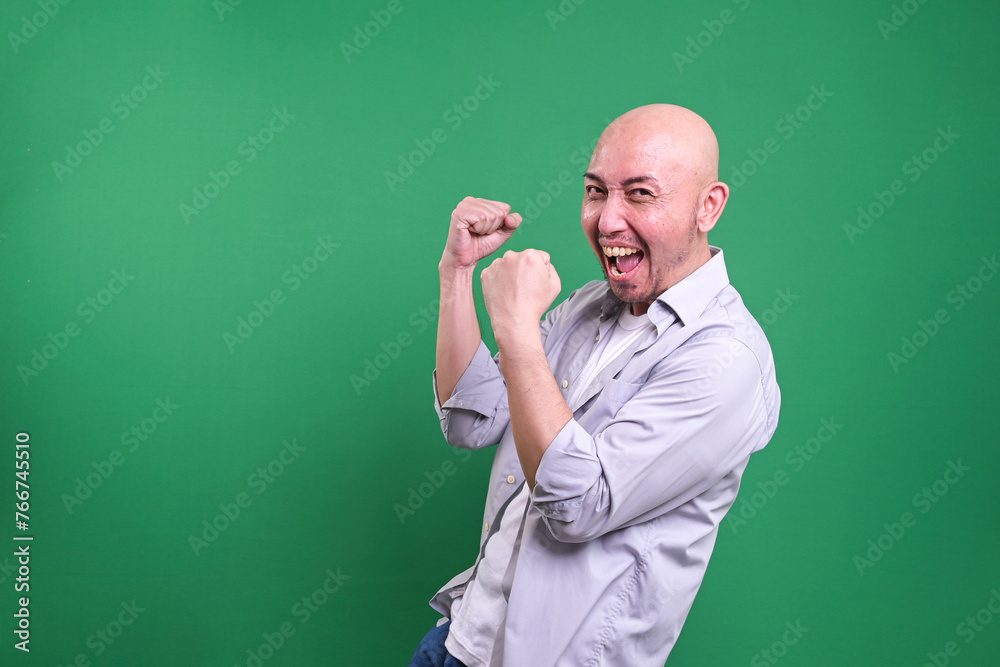 Portrait of satisfied bald man celebrating success over green background Portrait of satisfied bald man celebrating success over green background