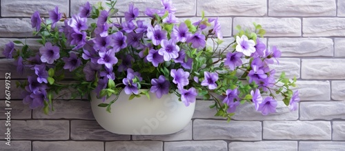 There is a white vase with purple flowers on it placed against a brick wall