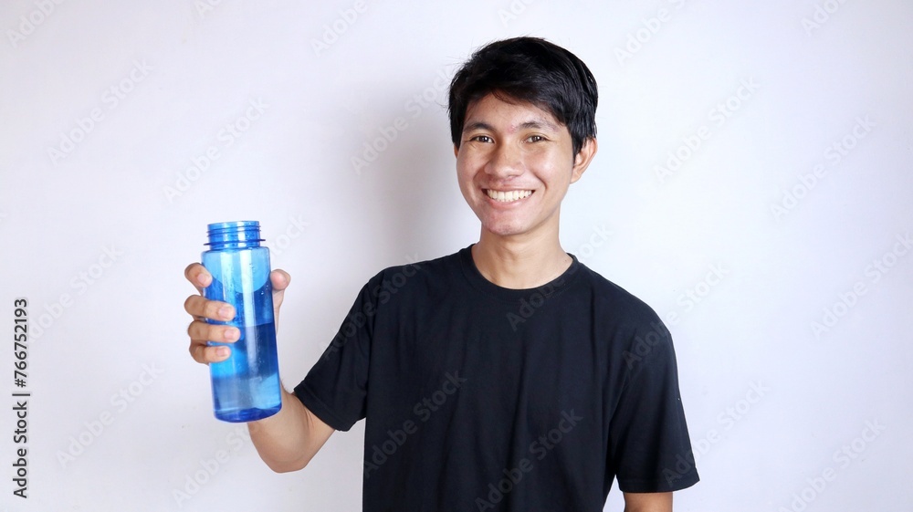 Handsome young Asian man smiling gesturingly holding a drinking water bottle Handsome young Asian man smiling gesturingly holding a drinking water bottle