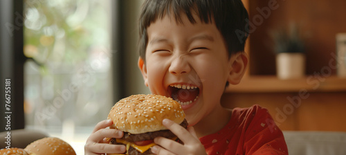 Excited asian little boy enjoying a delicious oversized burger at home