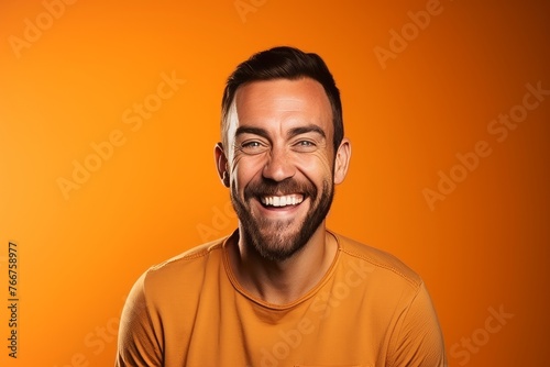 Portrait of a handsome man laughing and looking at camera on orange background © Inigo