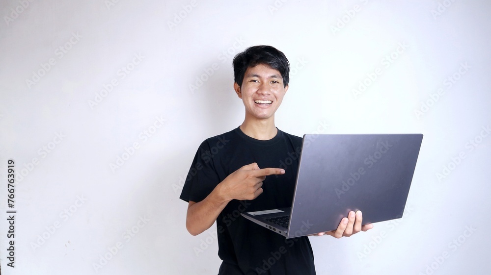 Excited young Asian man with gestures holding a laptop while pointing at the laptop