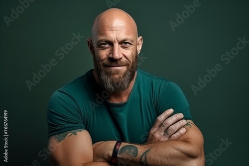 Portrait of a mature man with tattoos on his arms against a green background