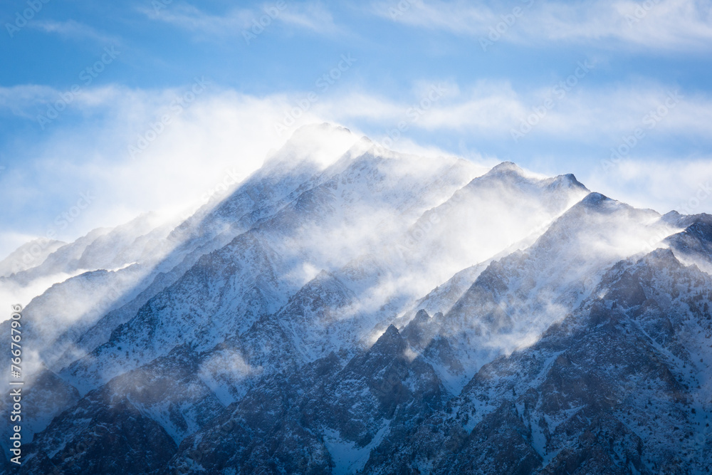 A closeup view of a mountain peak covered in snow as the wind swirls clouds around it. Aspen Springs, California - Highway 395