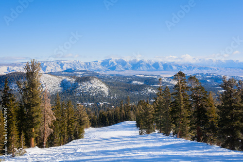 An empty, snowy ski slope with a view of snow-capped mountains in the distance. Mammoth Lakes, California