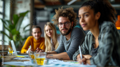 A multiethnic group of young professionals is engaged in a collaborative discussion at a brightly-lit, contemporary office setting, surrounded by project materials and workstations - Generative AI