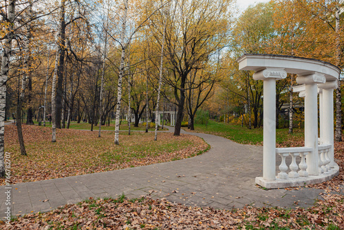 A path in an autumn park with a white gazebo in the background.