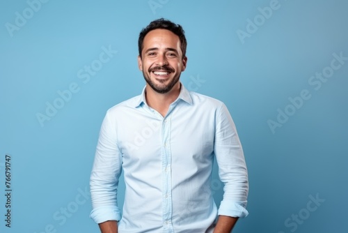 Portrait of a handsome young man smiling with hands in pockets on blue background