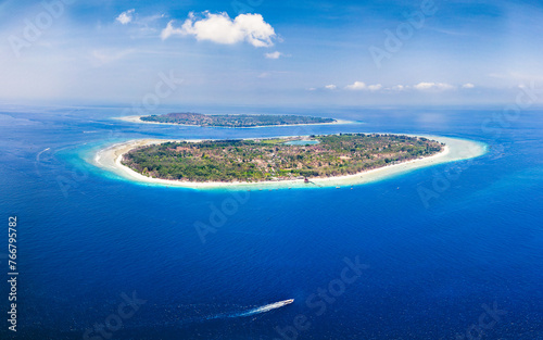 Aerial view of a small boat passing a tropical island in a blue ocean (Gili Meno)