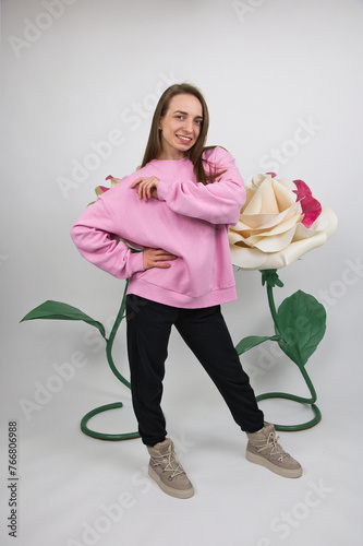 A girl in sportswear smiles against the background of large artificial roses. studio shot