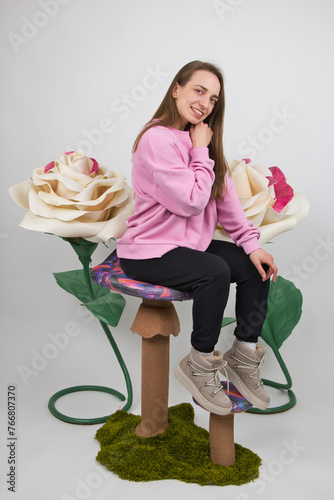 A girl poses with a smile against the background of large artificial white roses. studio shot