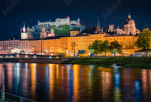 Old town of Salzburg reflected in Salzach river. Illuminated night cityscape of Salzburg with Hohensalzburg Castle on background. Austria, Europe. Traveling concept background.