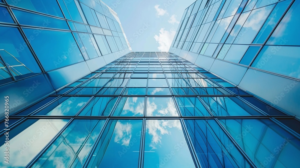 Obraz premium bottom-up perspective of a modern office building featuring blue sky and glass facades illustrating business activity and financial economy in urban setting