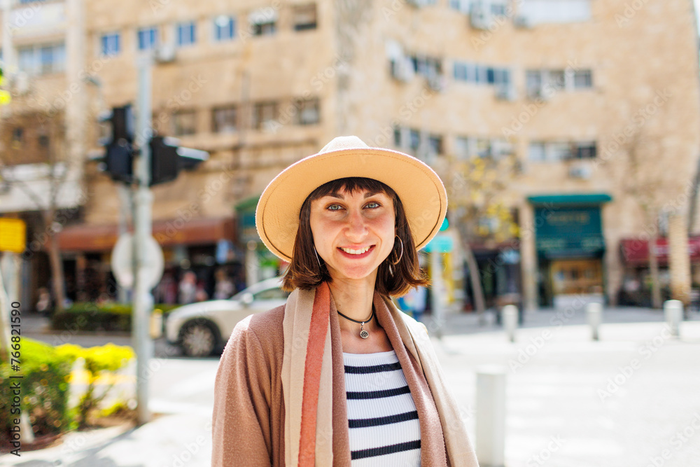 portrait of a cheerful white woman in a hat against the backdrop of the city in sunny weather. Travel to interesting places.
