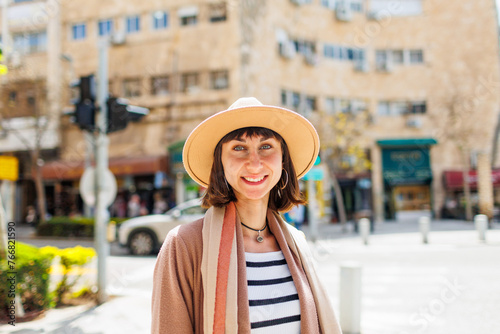portrait of a cheerful white woman in a hat against the backdrop of the city in sunny weather. Travel to interesting places. © zhukovvvlad