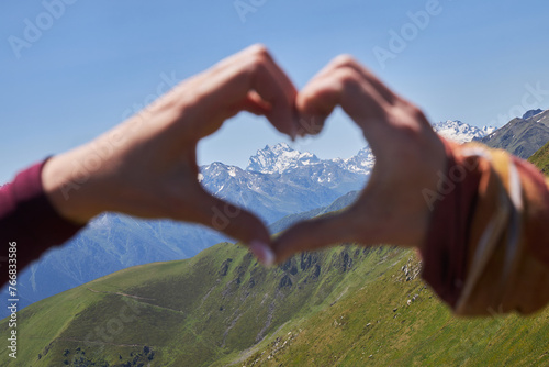 Two hands create a heart shape, capturing a view of snowy mountains in the distance