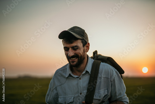 Trendy male wanderer strolling through open fields during twilight