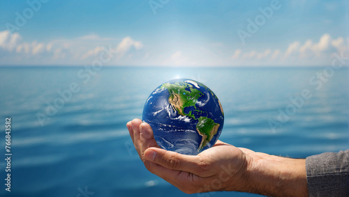 A hand holding a globe of the Earth against a background of blue sky and ocean. 