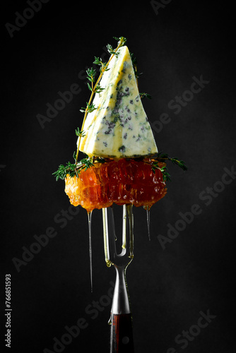 A piece of blue cheese with honeycombs. On a fork. Aged elite cheese.