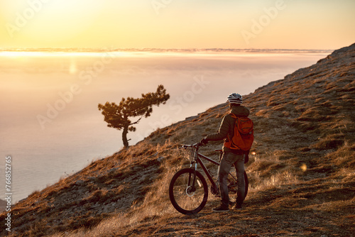 Sporty man athlete is standing with mtb bike at mountaintop and enjoys sunset or sunrise