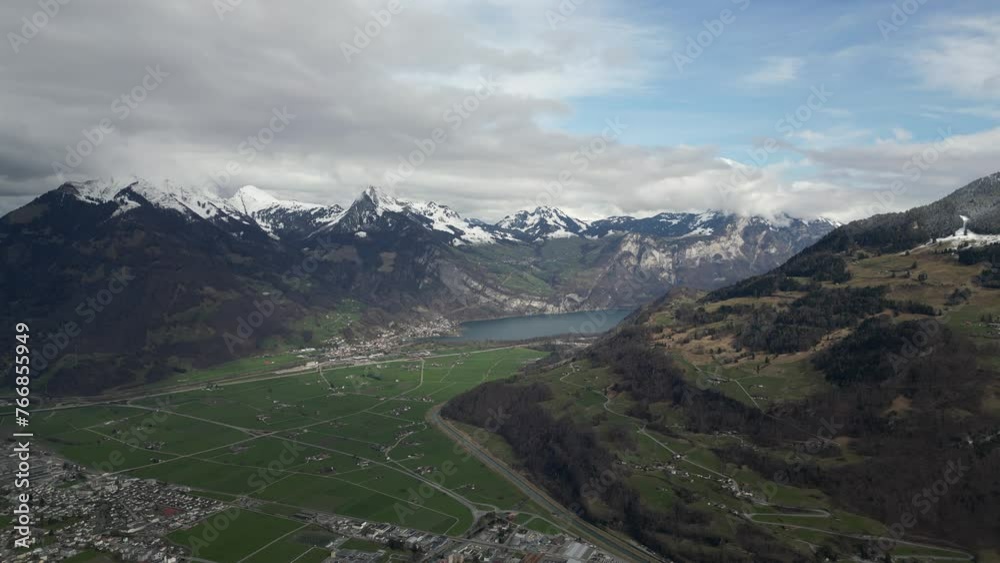 A high-altitude aerial of Glarus, Switzerland, reveals its surroundings enveloped by snow-capped mountain peaks, with a serene lake adding to the picturesque backdrop. A high-altitude aerial of Glarus, Switzerland, reveals its surroundings enveloped by snow-capped mountain peaks, with a serene lake adding to the picturesque backdrop.